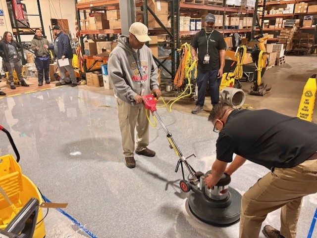 Trainer working hands-on with a crew member on a floor machine